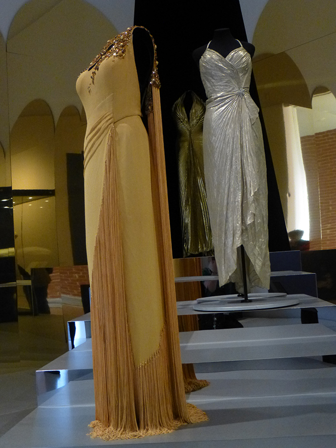 (foreground) Charles Le Maire (1897-1985), designer, Evening gown (1952), silk, bugle beads, fringing; originally made for The Snows of Kilimanjaro (Henry King, 1952); worn by Monroe in publicity photos, 1953. (middle) William (Jack) Travilla (1920-90), designer, Evening gown (1953), silver lamé; made for Gentlemen Prefer Blondes (Howard Hawks, 1953); worn by Monroe to the Los Angeles Herald Examiner Charity Event, 1953 and the Photoplay Magazine Awards,1954. (Collection of Greg Schreiner, Los Angeles). (rear) Gold lamé gown (replica) of one designed by Travilla, worn by Monroe in Gentlemen Prefer Blondes. (Americana Silver Screen Collection, Los Angeles). Installation photo: Inga Walton.